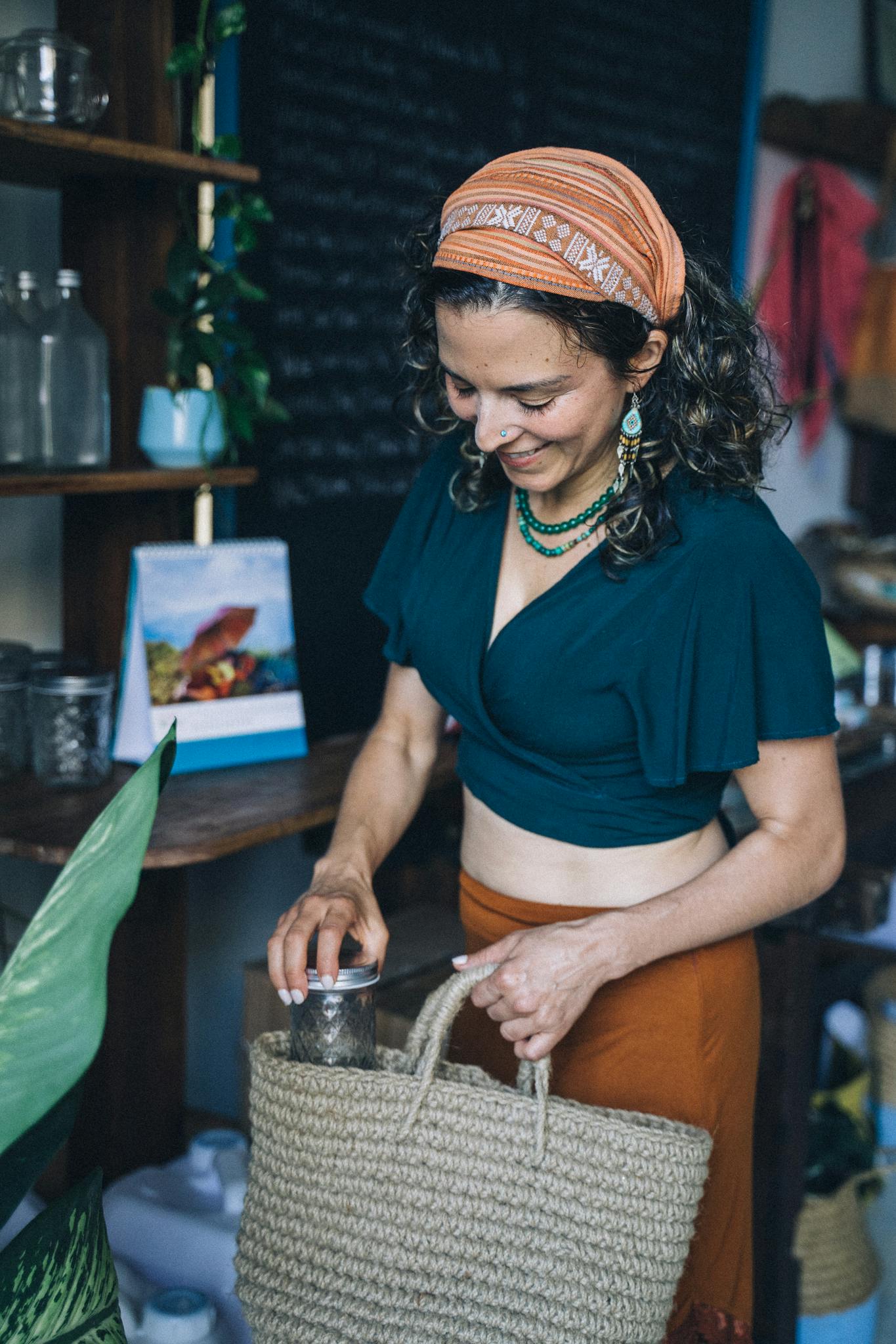 Smiling woman shops sustainably, filling a woven bag with eco-friendly products indoors.